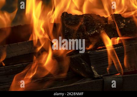 Ein brennendes Feuer im Dunkeln. Entzündung von Holz im Feuer. Eine helle brennende Flamme. Funken und Flammen im Dunkeln. Glühende Hitze und Kohlen und Flammen. Ein brennendes Lagerfeuer. Stockfoto