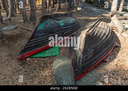 Zwei alte Fischerboote liegen am Ufer des Bergseeufers im Wald. Umgedrehte Holzboote auf dem Küstenstreifen oder der Küste. Küstenlinie Stockfoto