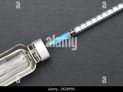 Flüssige Medizin in Fläschchen und Injektionsspritze auf dunkelgrauem Hintergrund Stockfoto