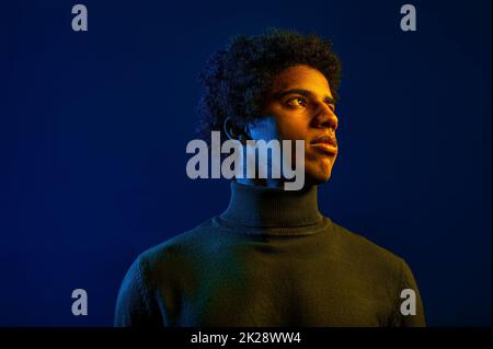 Junger ernsthafter Mann, der über dunklen Studiohintergrund hinweg blickt Stockfoto