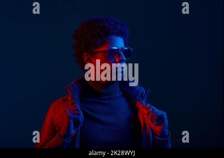 Ein selbstbewusster Mann zieht eine Jacke über dunklem Hintergrund an Stockfoto