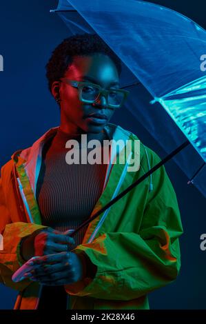 Hipster Frau im Regenmantel mit Regenschirm in Neonlicht Stockfoto