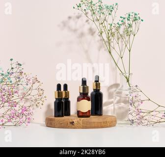 Braune Glasflasche mit einer Pipette auf einem Holzpodium und einem Blumenzweig. Werbung und Werbung für kosmetische Mittel Stockfoto