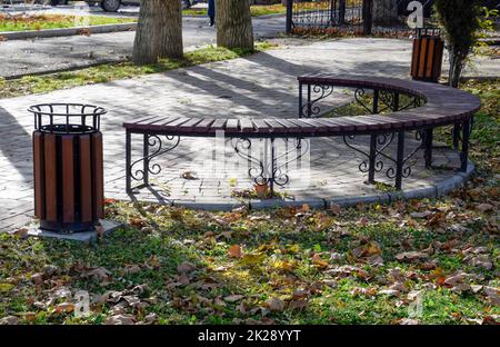 Bank in einem Herbstpark. Pflaster mit Fliesen und Mülltonnen. Stockfoto