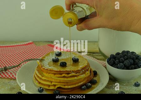 Nahaufnahme des Gießens von Ahornsirup auf den Stapel von Pfannkuchen. Stapel von Pfannkuchen mit frischen Heidelbeeren, gefüllt mit Ahornsirup Stockfoto