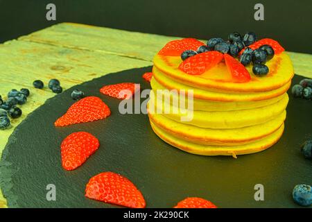 Pfannkuchen mit Früchten Beeren auf schwarzem Hintergrund. Frische Pfannkuchen. Heidelbeeren, Erdbeeren auf Pfannkuchen. Schiefer und Holzhintergrund Stockfoto