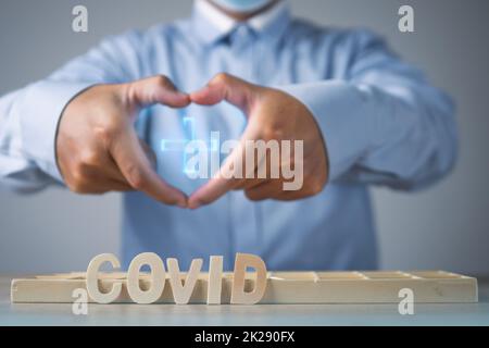 Broker präsentiert die Covid-Versicherung. Herzform mit den Händen. Holztexte liegen auf dem Tisch. Mittlere Nahaufnahme. Stockfoto