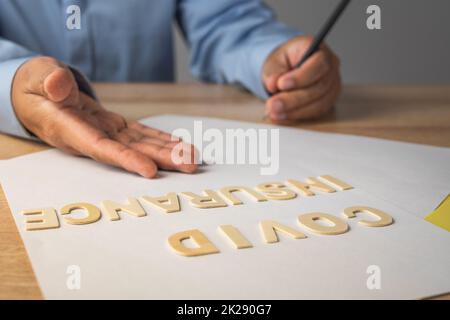 Broker präsentiert die Covid-Versicherung. Holztexte auf den Dokumenten. Mittlere Nahaufnahme mit Kopierbereich. Stockfoto