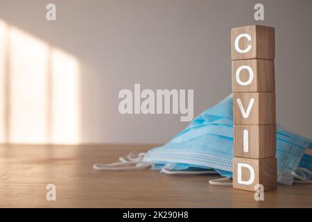 Dieses Konzept zeigt die Kampagne für das richtige Tragen der Maske. Holzblöcke mit Text, COVID. Blaue medizinische Maske auf dem Tisch. Krankheitsschutz wie Influenza, Grippe, Covid, Staub, PM2,5. Stockfoto