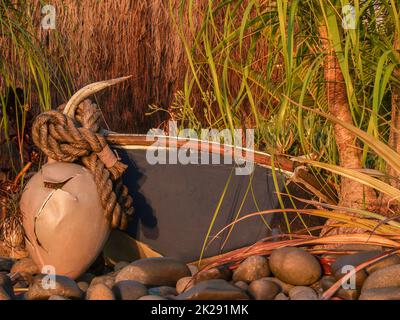 In der Nähe des nautischen Gartens befindet sich ein altes Boje-Boot und ein Anker, umgeben von Grün und Steinen im Morgenlicht. Stockfoto