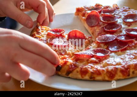 Kinderhände halten ein Stück Pizza Salami mit heißem Dampf und köstlichem Käse essen Freude die italienische Delikatesse in Makroansicht Nahaufnahme als ungesunder Snack mit Kalorien für Diät Fast Food Mahlzeiten Stockfoto