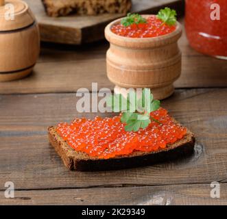 Kaviar aus rotem Lachs liegt auf einem Stück Roggenbrot. Brauner Holztisch Stockfoto