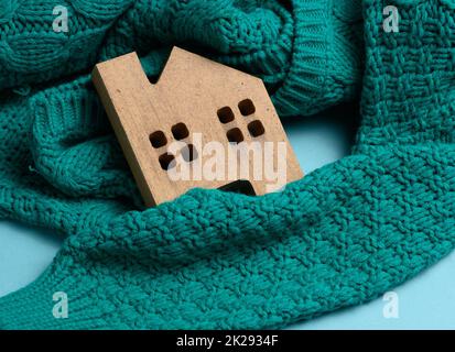 Das braune Holzmodell des Hauses ist in einen warmen Strickpullover gewickelt. Darlehenskonzept für Hautisolierung, alternative Energie Stockfoto