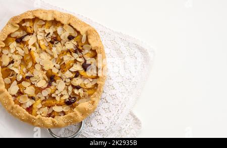 Gebackener, runder Kuchen mit Apfelstücken, mit Mandelflocken bestreut auf einem weißen Tisch Stockfoto