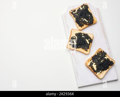 Paddelfischkaviar auf einer quadratischen Scheibe Weizenmehl-Brot auf einem hölzernen Schneidebrett. Draufsicht auf weißem Tisch Stockfoto