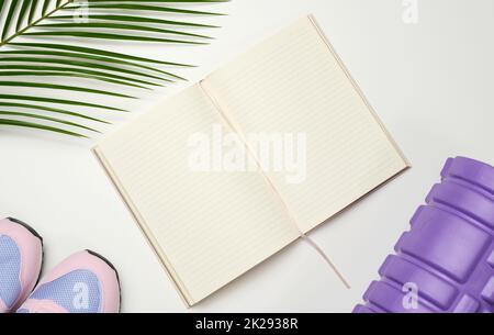 Offenes leeres Notebook, ein Paar Sportschuhe und Kurzhanteln auf weißem Hintergrund. Aufnahmeort, Draufsicht Stockfoto