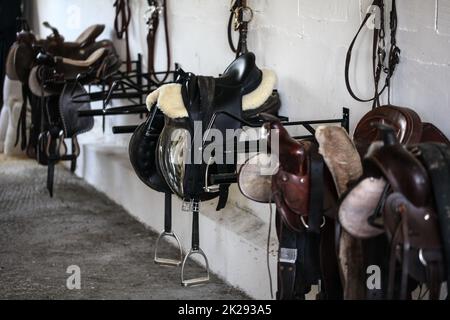 Leder Pferd Sättel und Ausrüstung auf Kleiderbügel im Sattelkammer Stockfoto