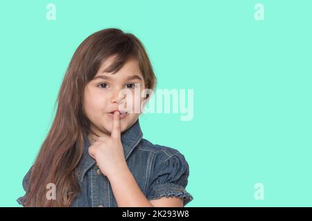 Das braune, langhaarige kleine Mädchen hält den Finger an die Lippen. Stockfoto