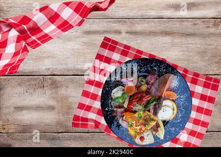Traditionelles italien-Essen. Nahaufnahme von gemischten mediterranen Vorspeisen oder Antipasto und Tapas mit Schinkengemüse und Krebs auf einem schwarzen Teller auf einem rustikalen Holztisch. Draufsicht. Stockfoto