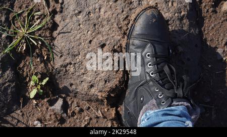 Frauen Stiefel im Schlamm, Detail von schmutzigen Stiefeln und schlammig, zu Fuß. Top down schmutzige schwarz geschnürte Stiefel Frau in blauen Jeans. Stockfoto