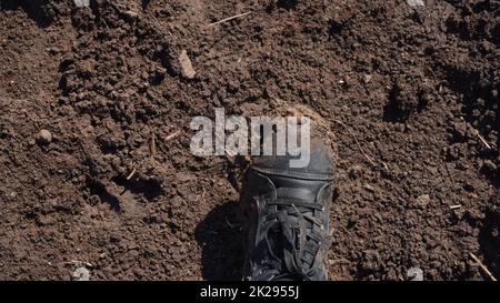 Frauen Stiefel im Schlamm, Detail von schmutzigen Stiefeln und schlammig, zu Fuß. Top down schmutzige schwarz geschnürte Stiefel Frau in blauen Jeans. Stockfoto