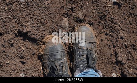 Frauen Stiefel im Schlamm, Detail von schmutzigen Stiefeln und schlammig, zu Fuß. Top down schmutzige schwarz geschnürte Stiefel Frau in blauen Jeans. Stockfoto