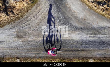 Luftaufnahme mit Drohne einer Radfahrerin auf der Straße mit Schatten Stockfoto