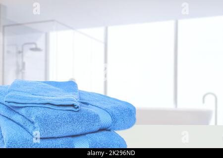 Tischplatte auf Handtuchhintergrund. Nahaufnahme eines Stapels oder Stapels blauer weicher Frottee-Badetücher an einem hellen Tisch vor abstraktem, verschwommenem Badezimmerhintergrund. Leerzeichen. Stockfoto