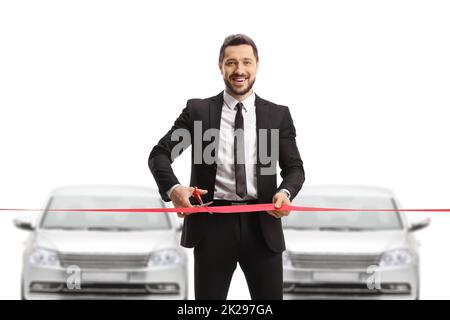 Manager in einem Anzug, der in einem Autosalon ein rotes Band schneidet und die Kamera auf weißem Hintergrund isoliert anlächelt Stockfoto