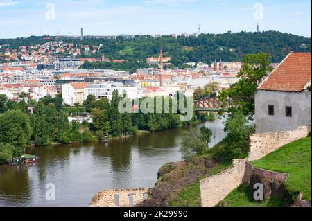 Die Bäume entlang der Moldau sind vom Hang aus durch die alte Ziegelmauer, die Teil des alten Verteidigungssystems ist, zu sehen. Der Himmel ist blau mit Wolken. Stockfoto