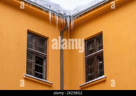 Eiszapfen hängen vom Dach des orangefarbenen Gebäudes Stockfoto