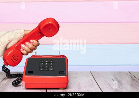 Eine feminine, elegante, wunderschön manikürte Frauenhand, die ein altes rotes Telefon über abstrakter, gestreifter Hintergrundstruktur hält. Kommunikationshintergrund. Leerzeichen. Stockfoto