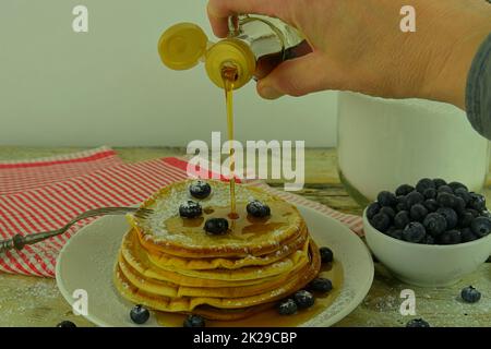 Nahaufnahme des Gießens von Ahornsirup auf den Stapel von Pfannkuchen. Stapel von Pfannkuchen mit frischen Heidelbeeren, gefüllt mit Ahornsirup Stockfoto