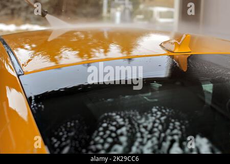 Top von gelben Auto in Waschstraße gewaschen, fließendes Wasser auf dem Dach und kleinen Antenne. Stockfoto