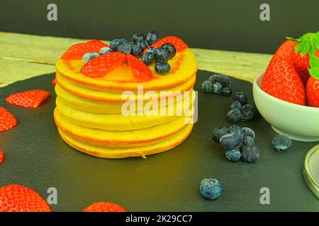 Pfannkuchen mit Früchten Beeren auf schwarzem Hintergrund. Frische Pfannkuchen. Heidelbeeren, Erdbeeren auf Pfannkuchen. Schiefer und Holzhintergrund Stockfoto