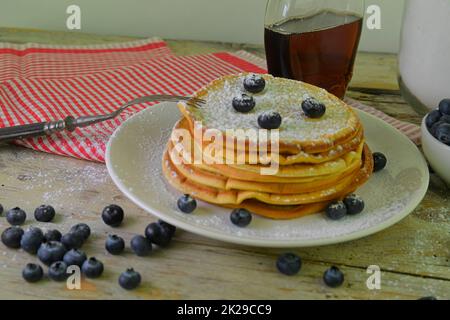 Köstliche Pfannkuchen mit frischen Blaubeeren und Sirup auf einem rustikalen Holztisch. Ahornsirup und Blaubeeren auf Pfannkuchen. Rustikaler weißer Tisch. Nahaufnahme Stockfoto