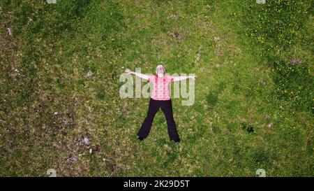 Drohnenaufnahme einer älteren Frau, die entspannt auf einer Bergwiese liegt Stockfoto