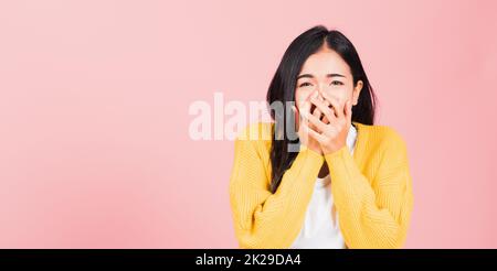 Asiatisches Porträt wunderschöne, süße junge Frau, die erstaunt steht, schockiert, mit dem Mund bedeckt, mit Gesten bedeckte Handflächen, die auf die Kamera blickten, Studio-Aufnahme isoliert auf pinkem Hintergrund, Thai-Frau verängstigt mit Kopierraum Stockfoto