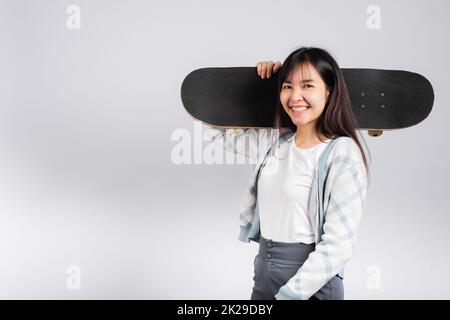 Lächelnde glückliche Frau, die Skateboard auf der Schulter hält