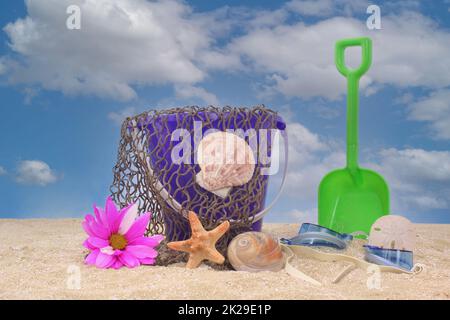 Sandeimer mit Netz und Meeresmuscheln auf Sand mit Himmelshintergrund Stockfoto