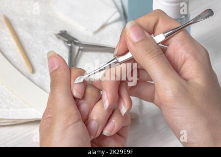 Maniküre. Die Nagelhaut mit einem Metalldrücker zurückschieben. Sich bei der Maniküre verletzen. Hautpflege, Hände, Nägel, Hygiene. Spa-Salon, Nagelsalon. Häusliche Pflege. Schönheit. Frauenhände Stockfoto