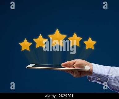 Eine weibliche Hand hält ein elektronisches Tablet und fünf gelbe virtuelle Sterne über dem Bildschirm. Benutzerbewertung der Anwendung, des Dienstes. Qualitätsbewertung Stockfoto