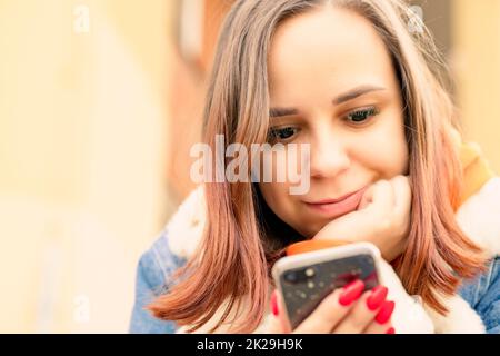 Porträt einer jungen Frau, die auf dem Mobiltelefon surft, sitzt und sich an der Hand lehnt. Nahaufnahme Stockfoto