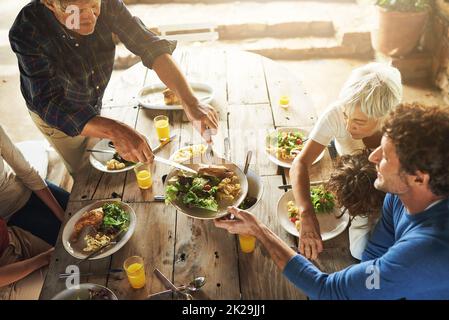 CMON alle, Dish up. Aufnahme einer Familie aus dem hohen Winkel zum gemeinsamen Mittagessen im Freien. Stockfoto