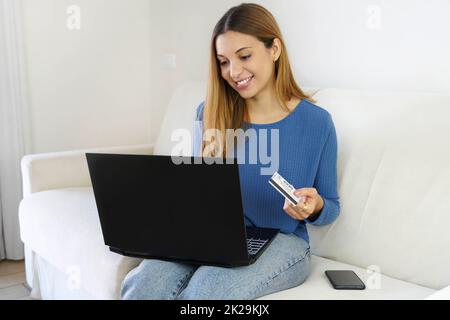 Brasilianisches schönes Mädchen, das online mit Kreditkarte und Laptop einkaufen kann, während es zu Hause auf dem Sofa sitzt Stockfoto