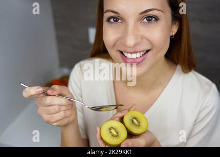 Schöne junge Frau, die lächelt und zu Hause goldene Kiwi-Früchte isst. Nahaufnahme von oben. Antioxidans, Vitamin C, gesundes Konzept. Stockfoto