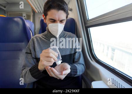 Fahren Sie sicher mit öffentlichen Verkehrsmitteln. Junger Mann mit Gesichtsschutzmaske desinfiziert Hände aus Alkohol-Gel-Spender. Passagier mit medizinischer Maske desinfizierende Hände im Zugwagen. Stockfoto