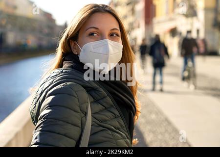 Porträt einer lässigen Frau mit KN95 FFP2 Schutzmaske dreht sich um und starrt in die Stadt Stockfoto