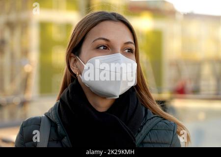 Hoffnungsvoll schöne Frau mit einer schützenden KN95 FFP2 Maske, die am Sonnenuntergang auf der Stadtstraße spazierengeht Stockfoto