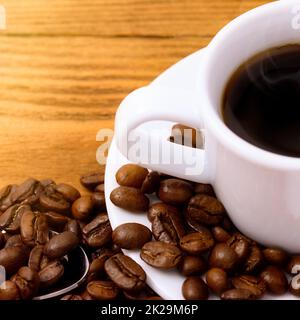 Eine Tasse Kaffee auf einem Holztisch mit verstreuten, frisch gerösteten Kaffeebohnen. Stockfoto